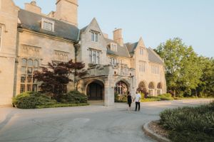 A grand stone mansion with Gothic architecture features and manicured landscaping at sunset.