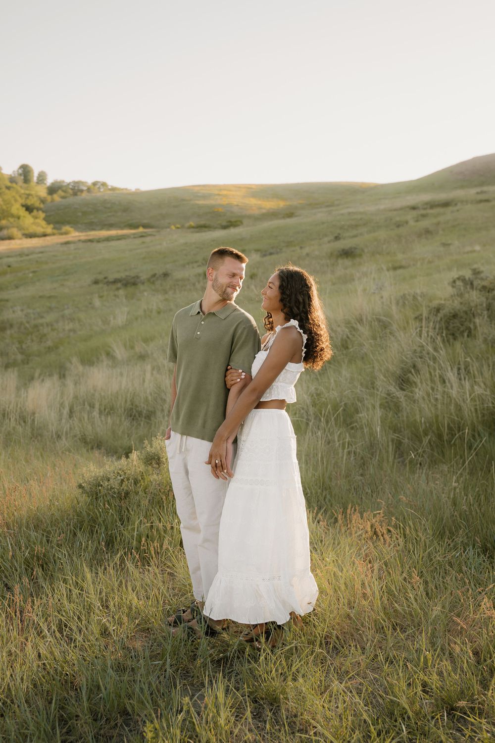 A couple shares an intimate moment while standing in a golden-lit hillside meadow.
