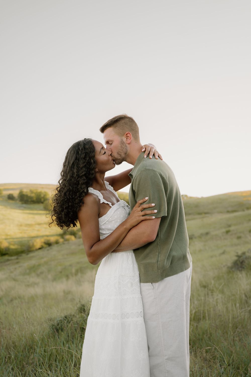 A romantic couple shares intimate moments in a grassy field during sunset in natural light photography.