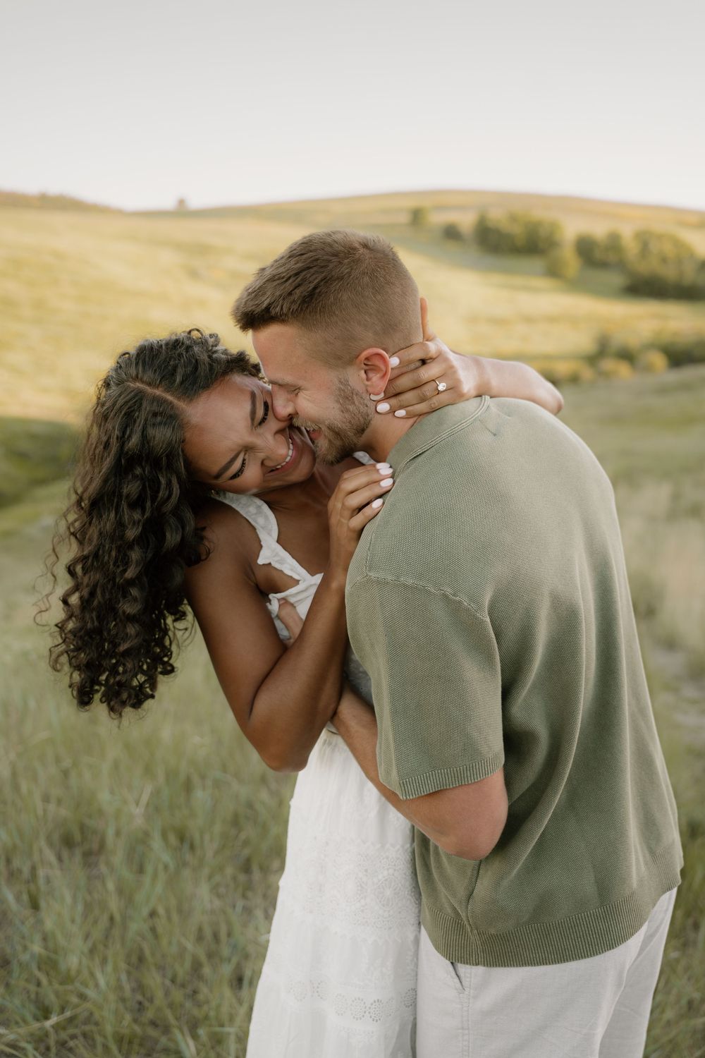 Intimate moment captured between couple laughing and embracing in golden mountain meadow.