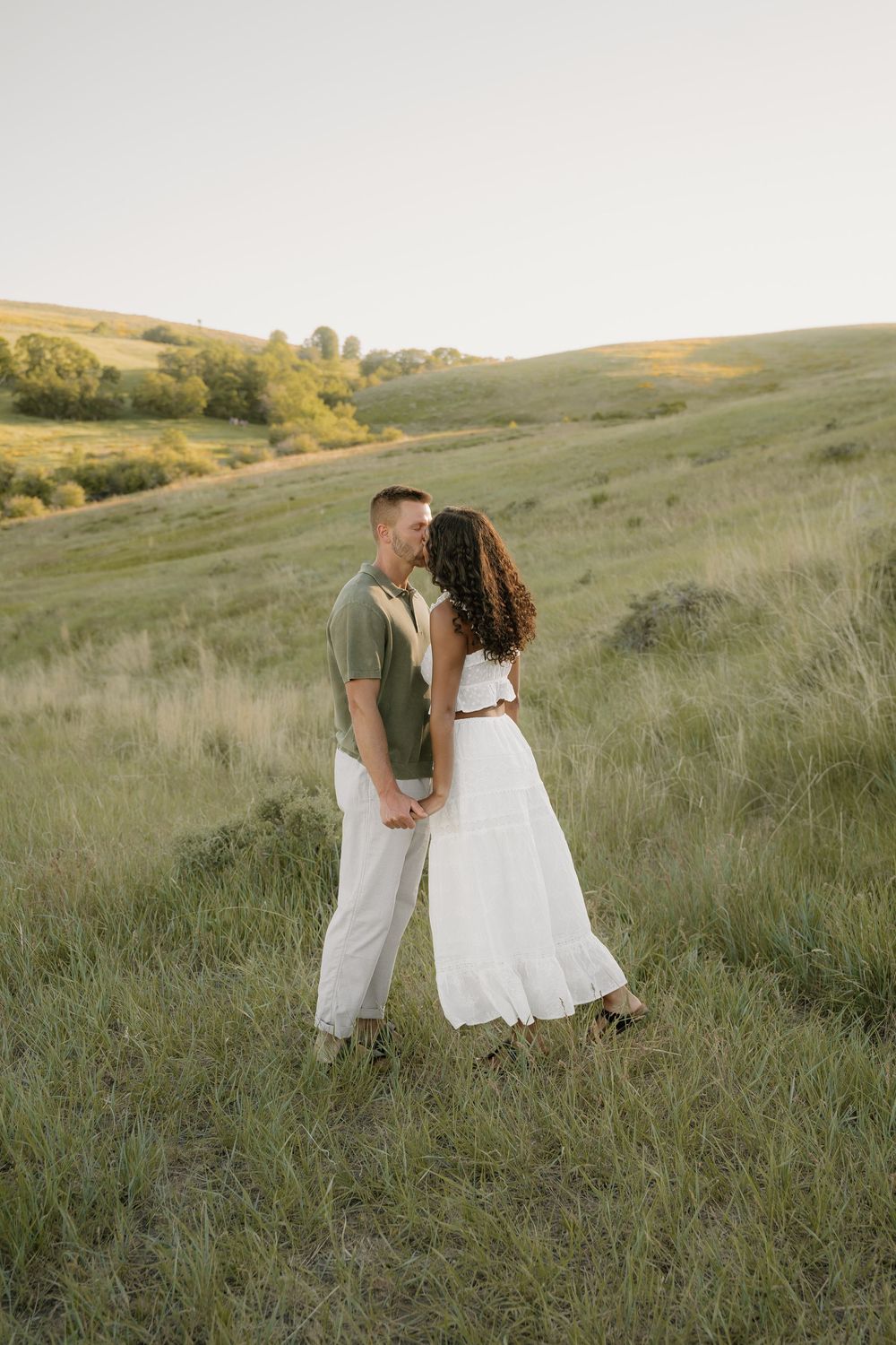 Couple sharing tender moments in a beautiful hillside field during sunset.