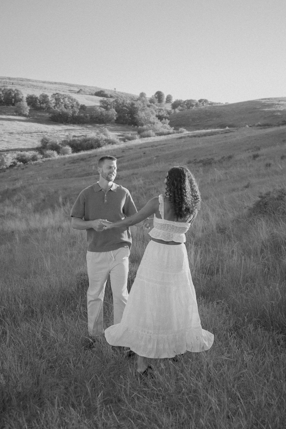 Black and white photo of couple walking hand in hand through rolling prairie landscape.