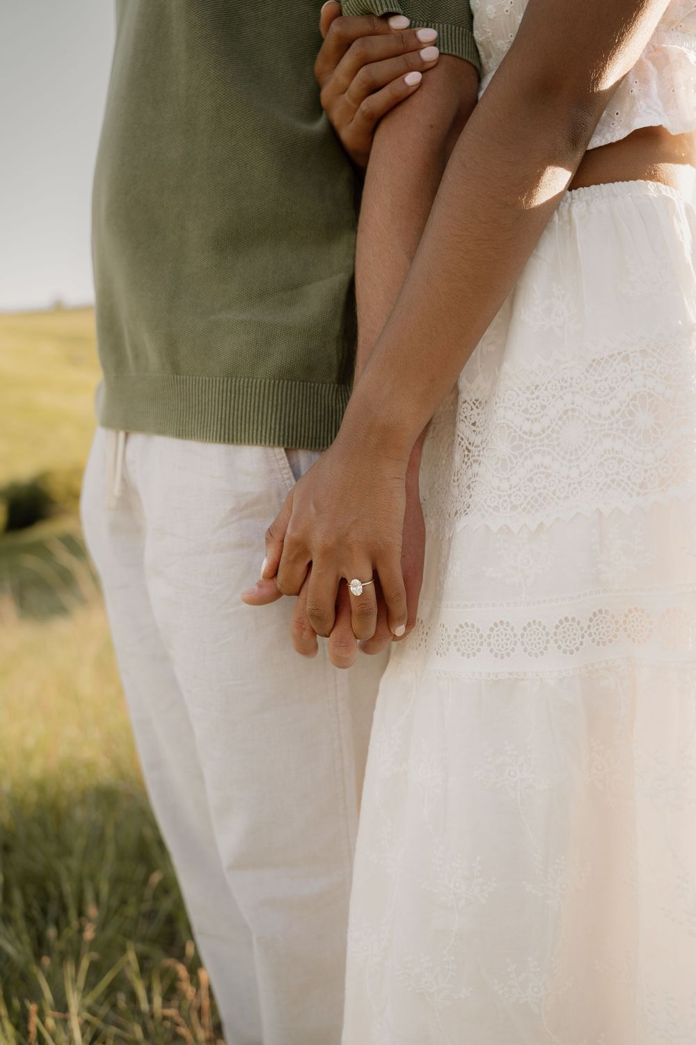 Close-up of a couple holding hands against a backdrop of rolling hills and golden grass.