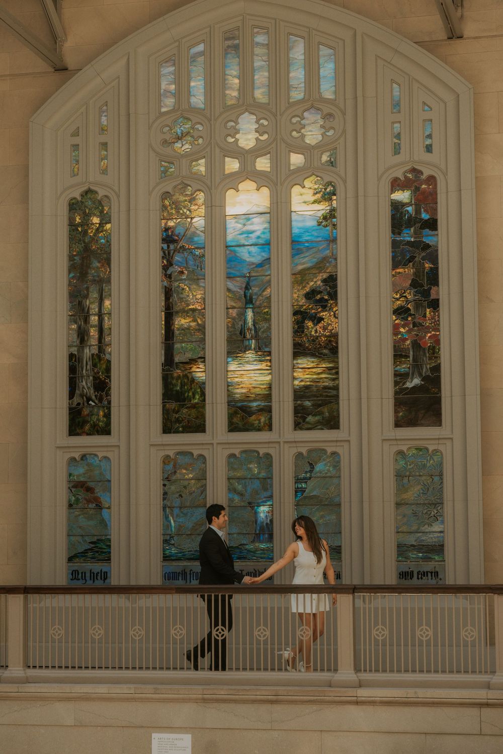 A couple stands in front of a stunning stained glass window inside a grand cathedral.