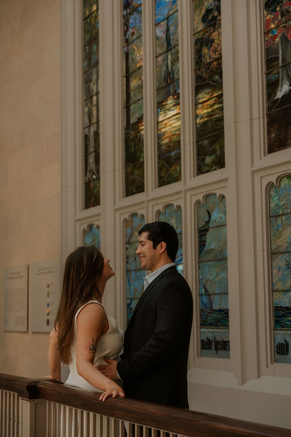 Couple standing by ornate stained glass windows in a historic building interior.