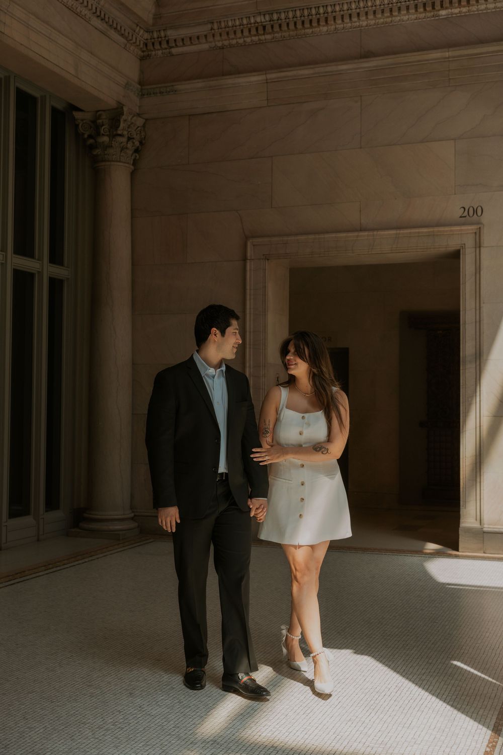 A couple in formal attire standing in an elegant hallway with classical architecture.