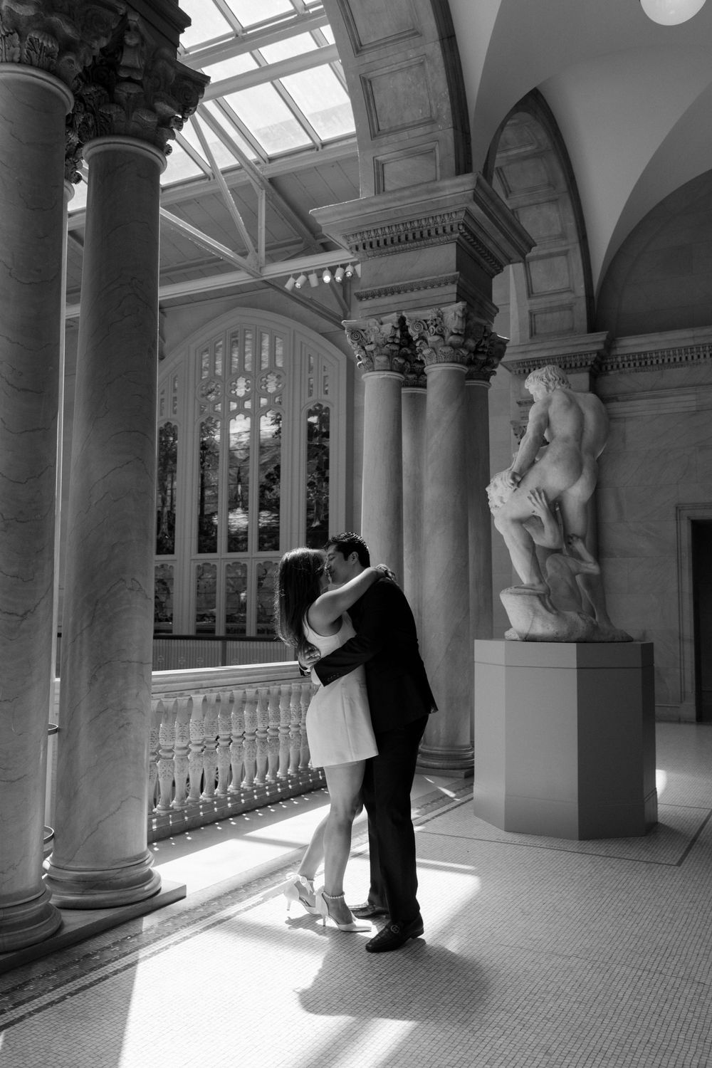 A romantic moment captured in a grand classical hallway with marble columns and a skylight.