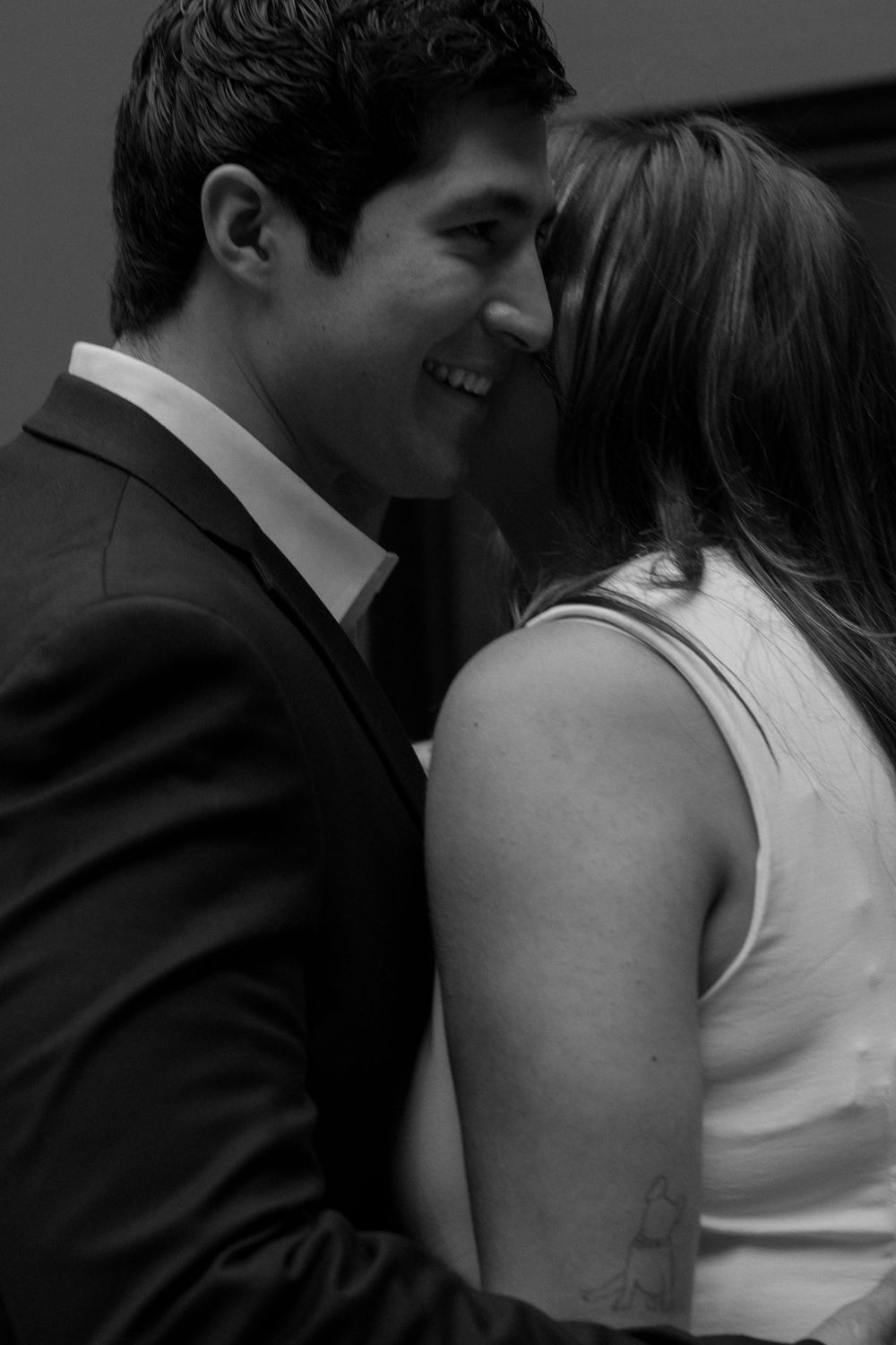 An intimate black and white photograph captures a tender moment between a couple in formal attire.