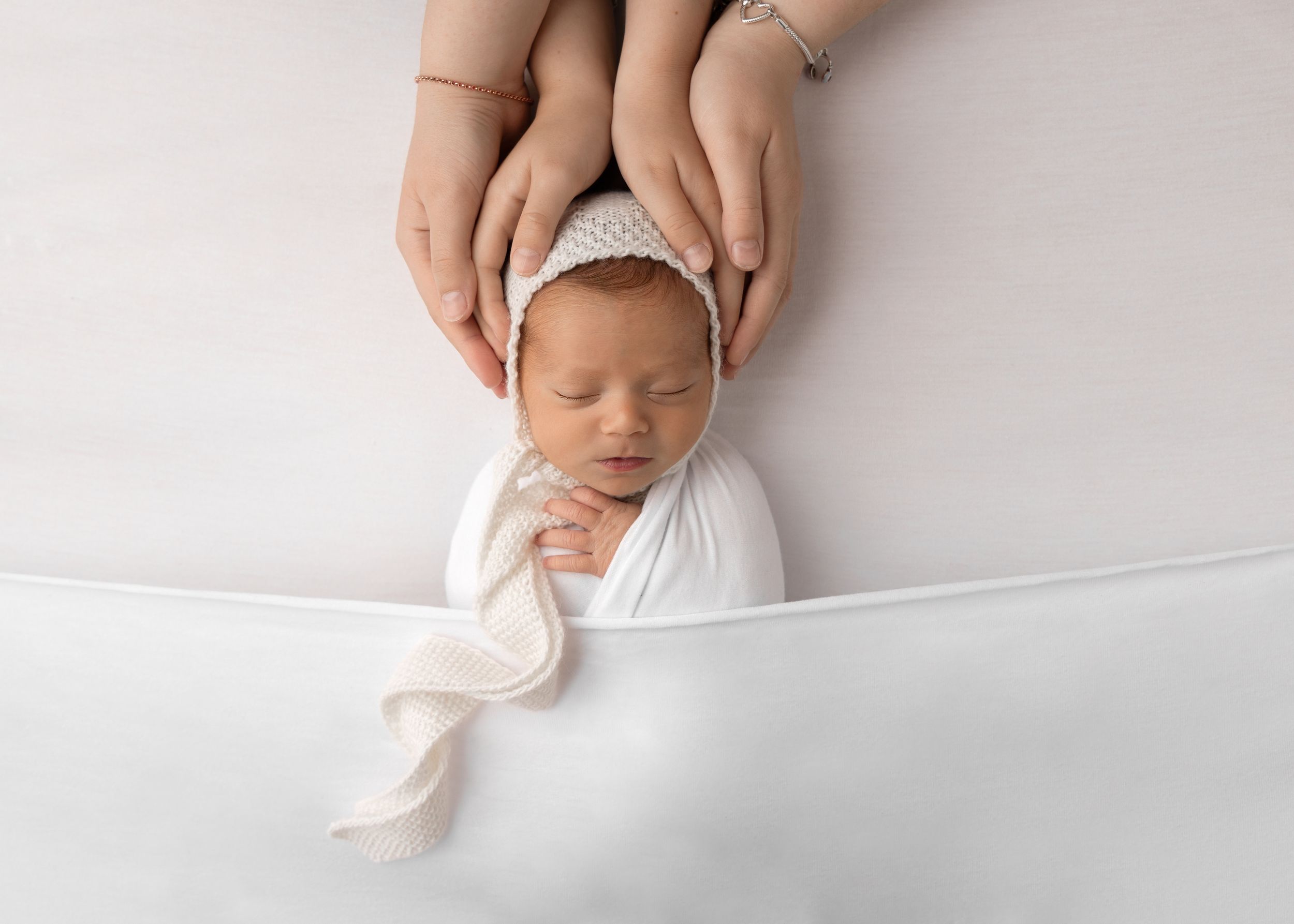 Newborn baby in white wrap and bonnet being gently cradled.