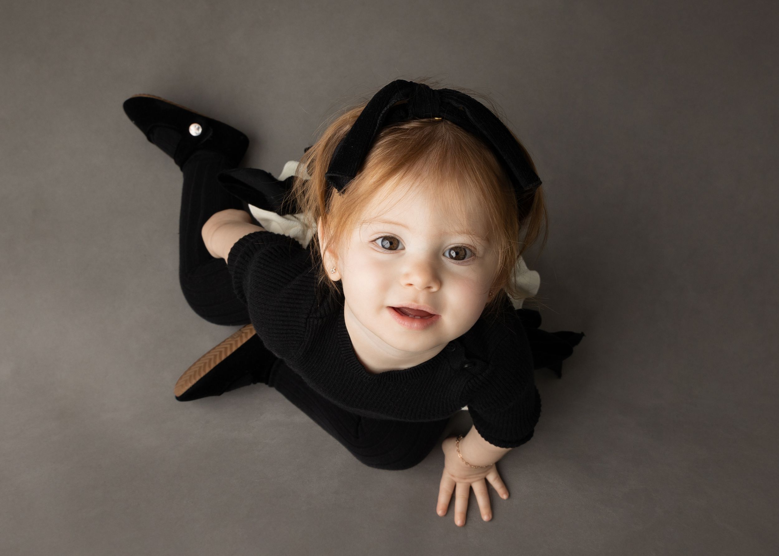 Small child in black bat costume lying on dark background.