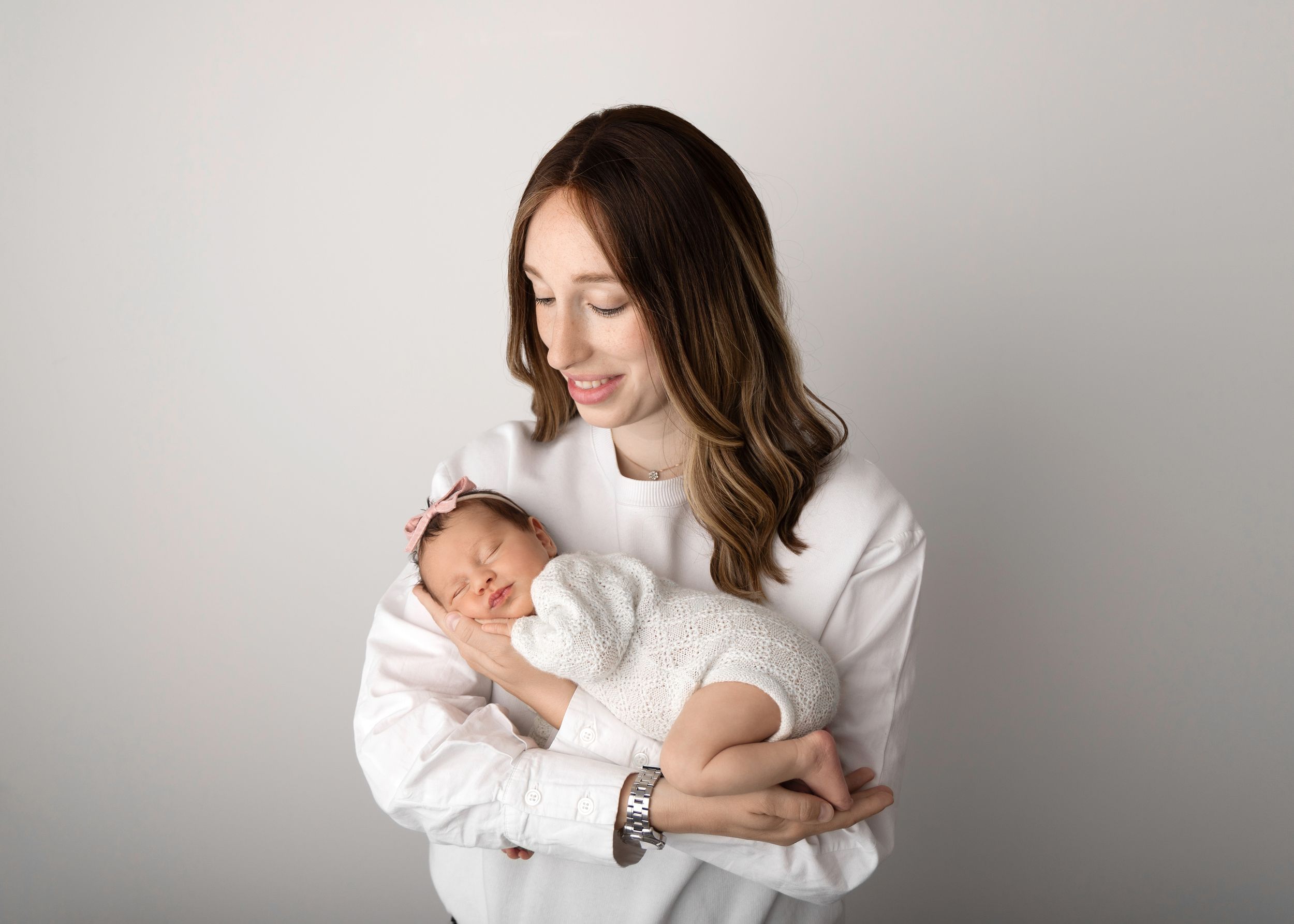 A tender moment showing a newborn baby being cradled in white against a neutral background.