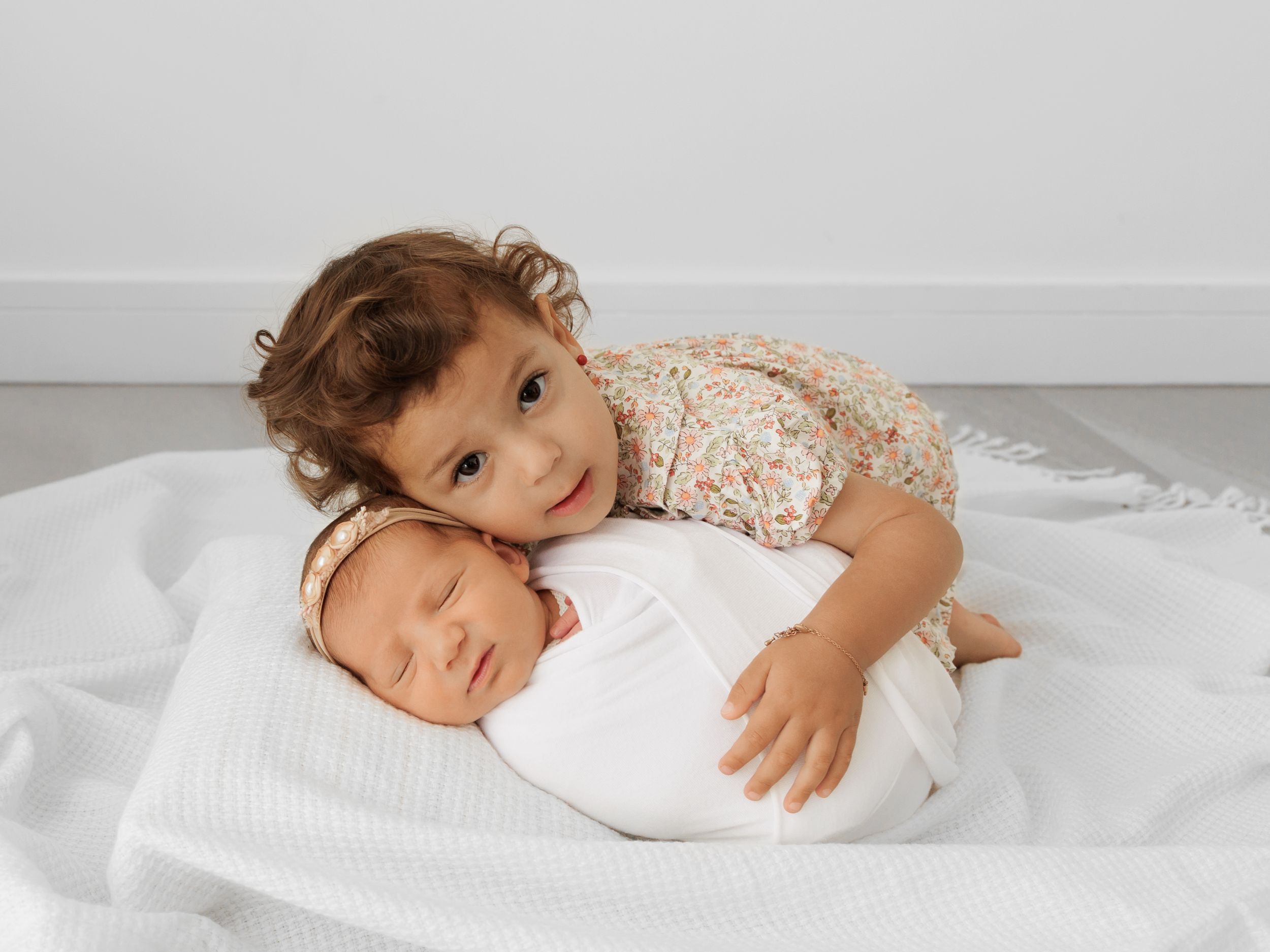 Two young children cuddling together on white bedding during photo session.
