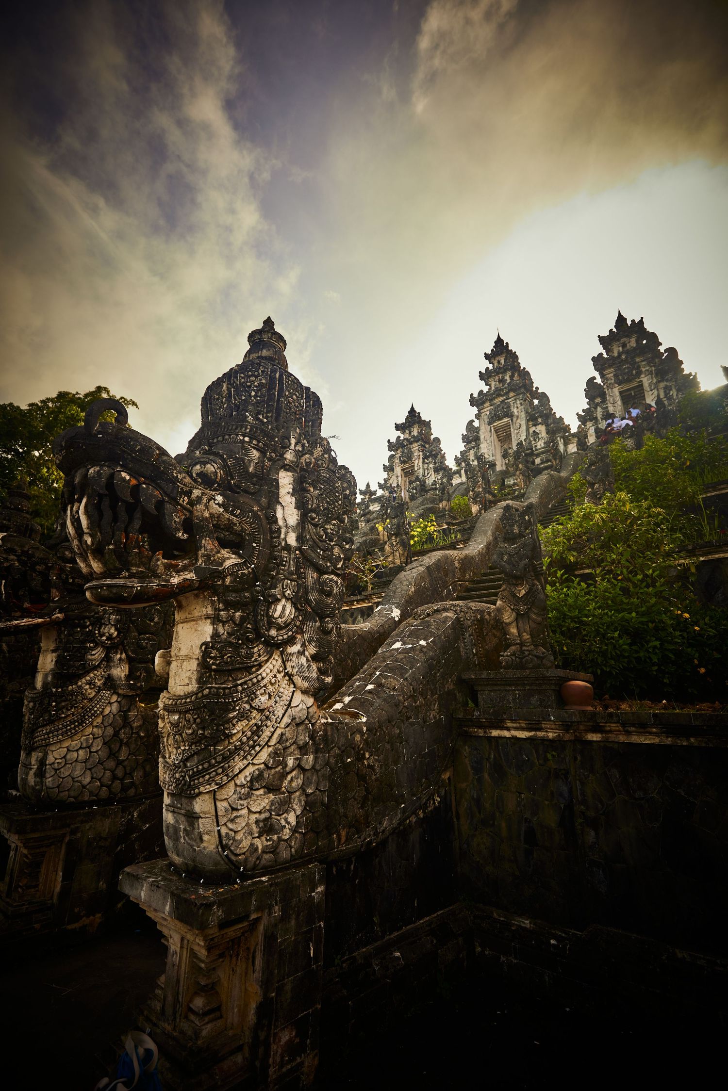 Ancient temple spires and structures under dramatic cloudy sky in Southeast Asia.