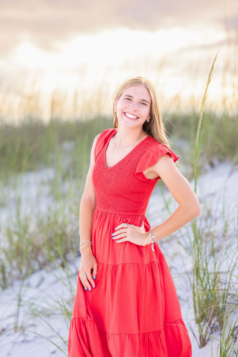 Bright red tiered maxi dress with v-neck worn on sandy beach with sea grass at sunset.