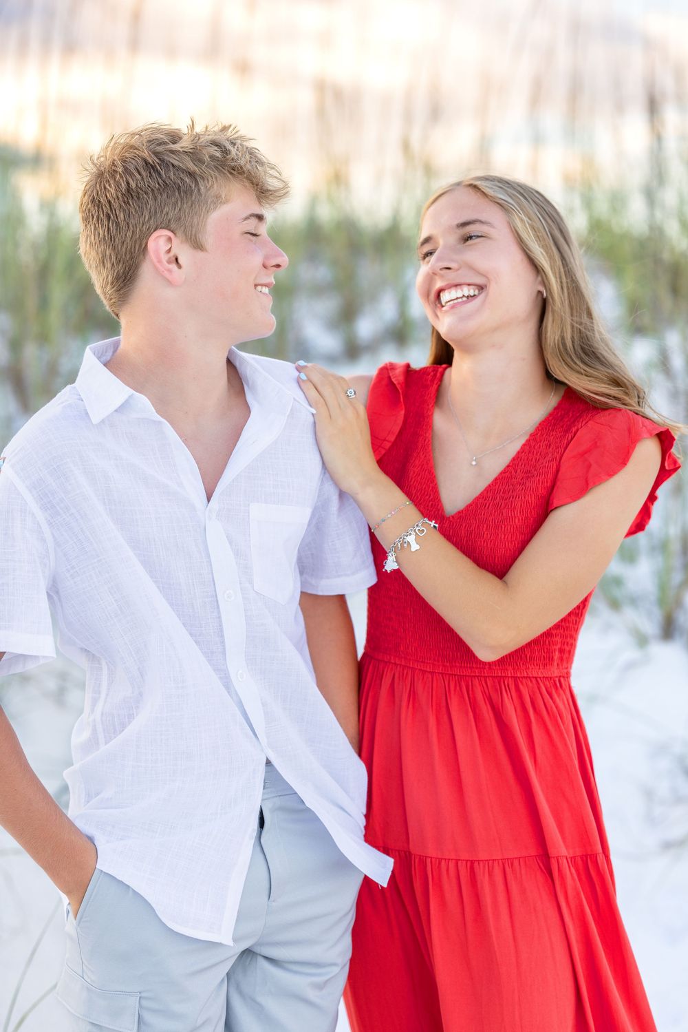 A couple in white and red outfits shares playful moments on a sandy beach in a series of romantic photos.