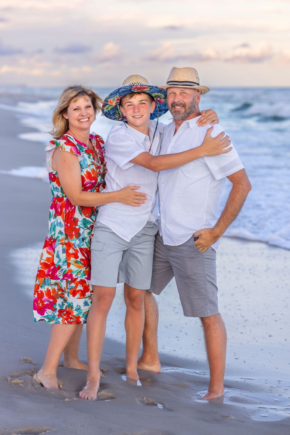 Three people pose together on a beach at sunset with waves in the background.