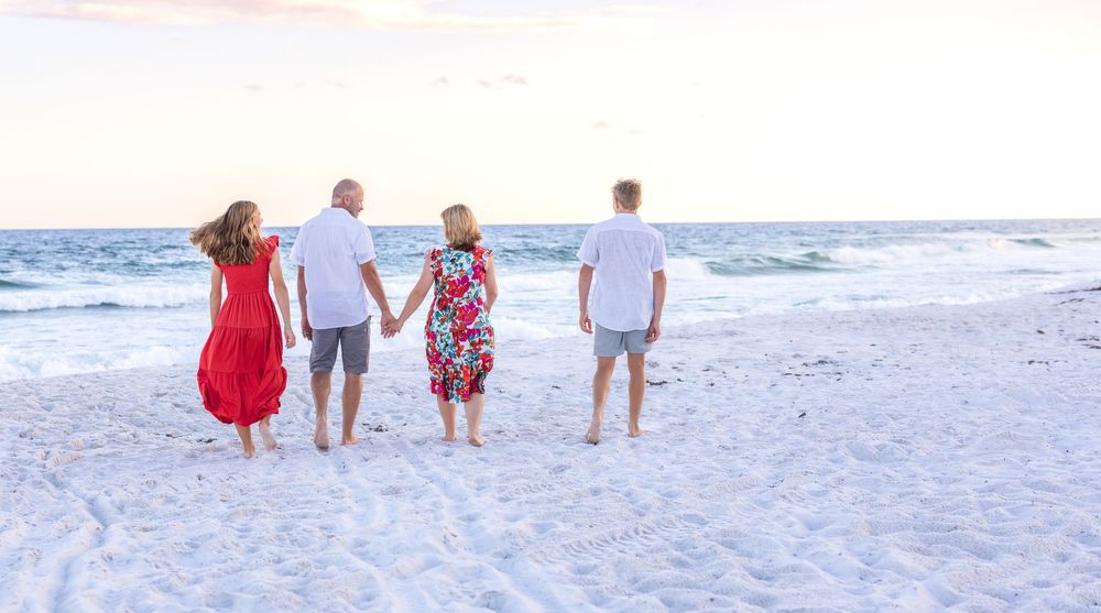 A family walks together along a white sandy beach at sunset with ocean waves in the background.