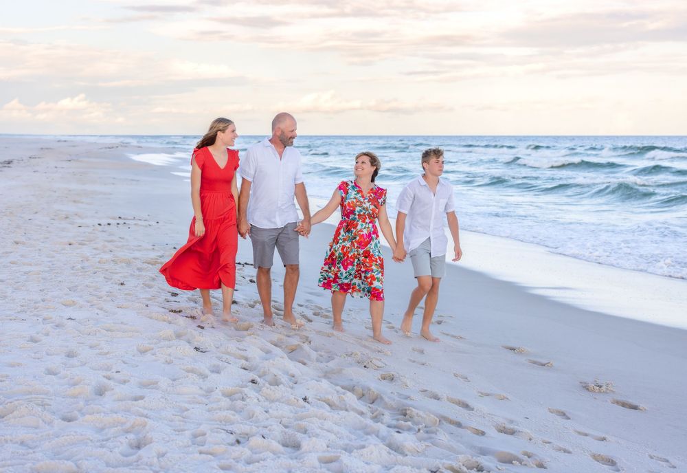A group of people walk along a sandy beach at sunset holding hands with ocean waves and soft pastel skies in the background.