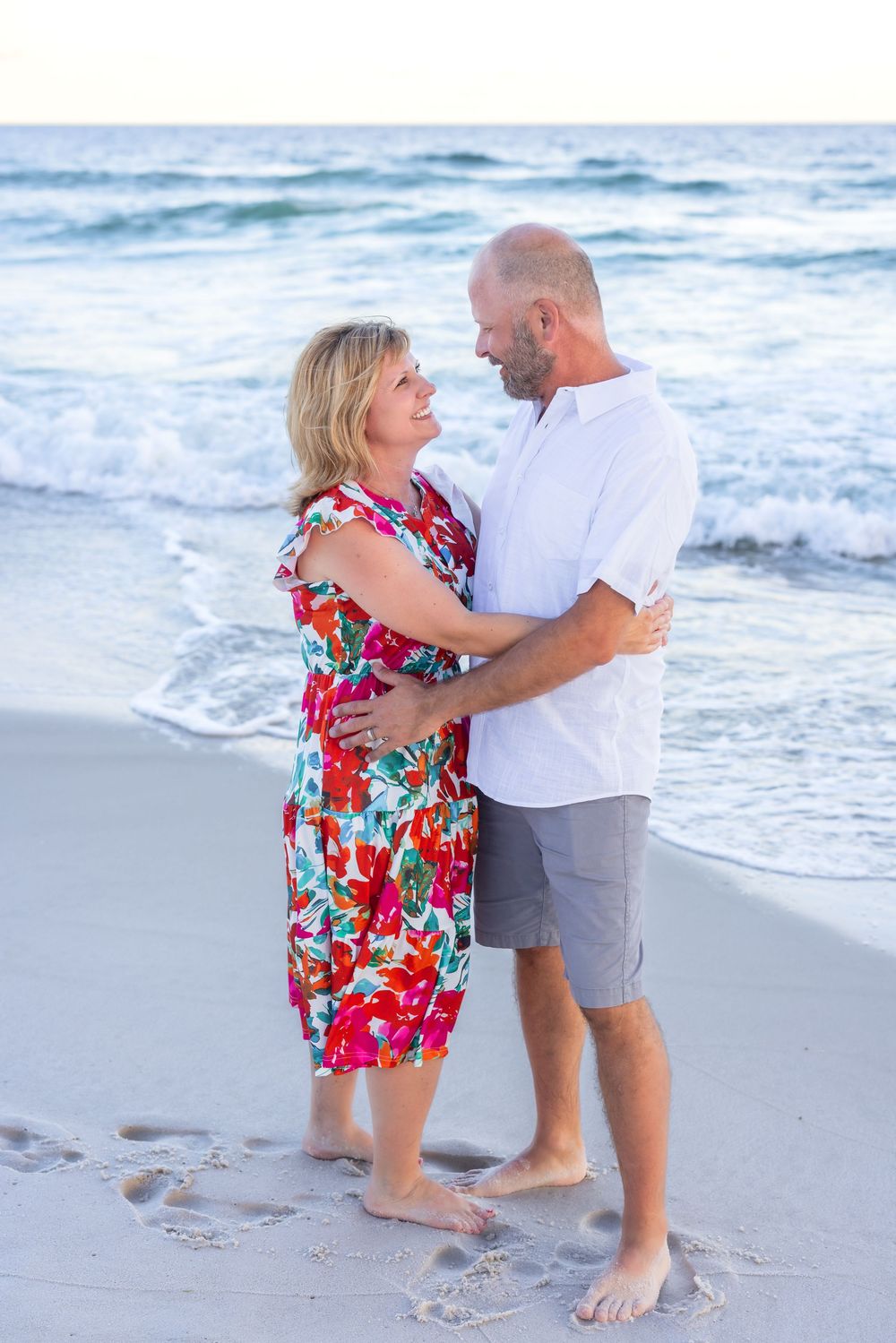 A couple in love dances and embraces on a sunny beach with waves crashing behind them.