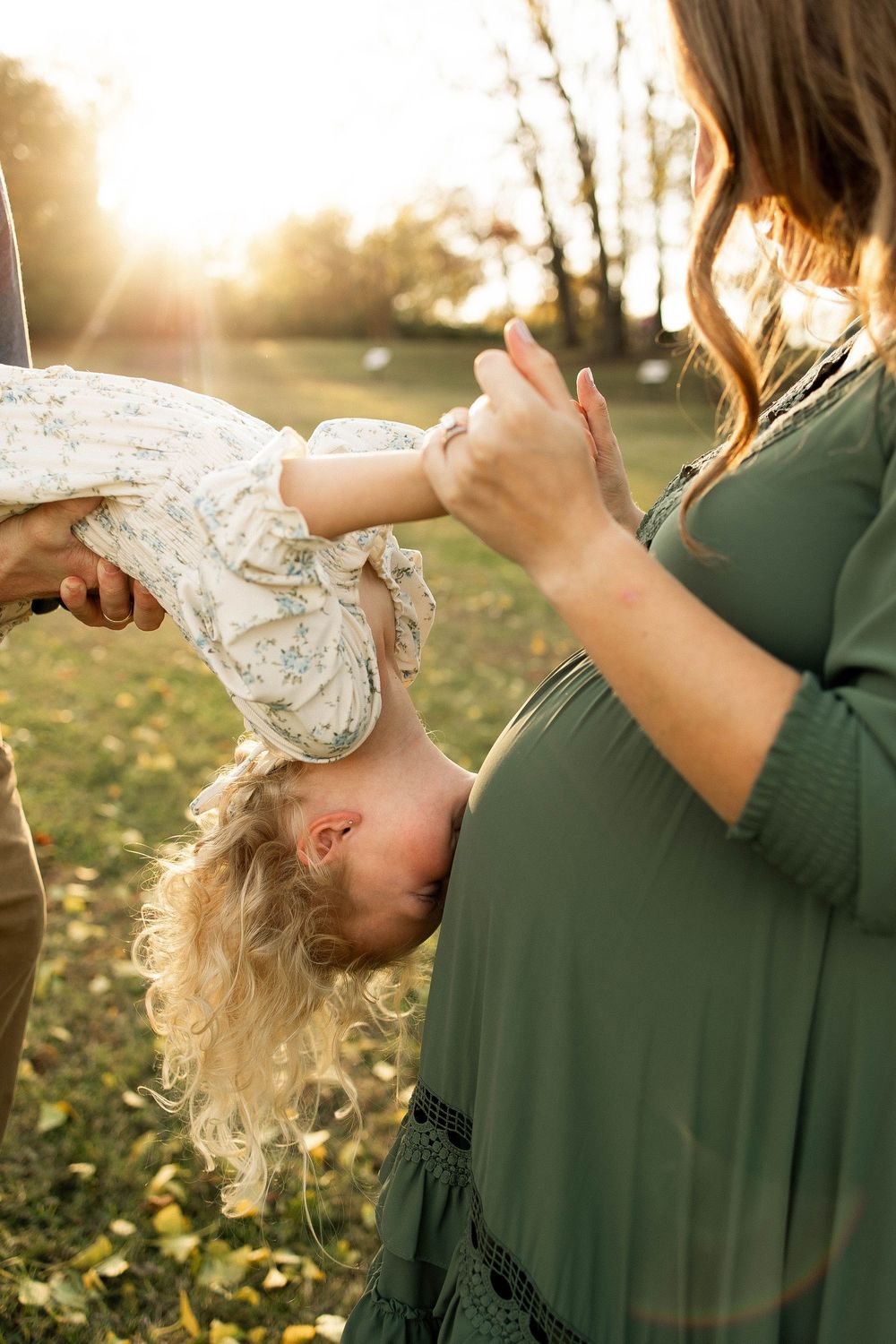 Parent and child share a tender moment in golden sunlight with autumn leaves scattered on the ground.