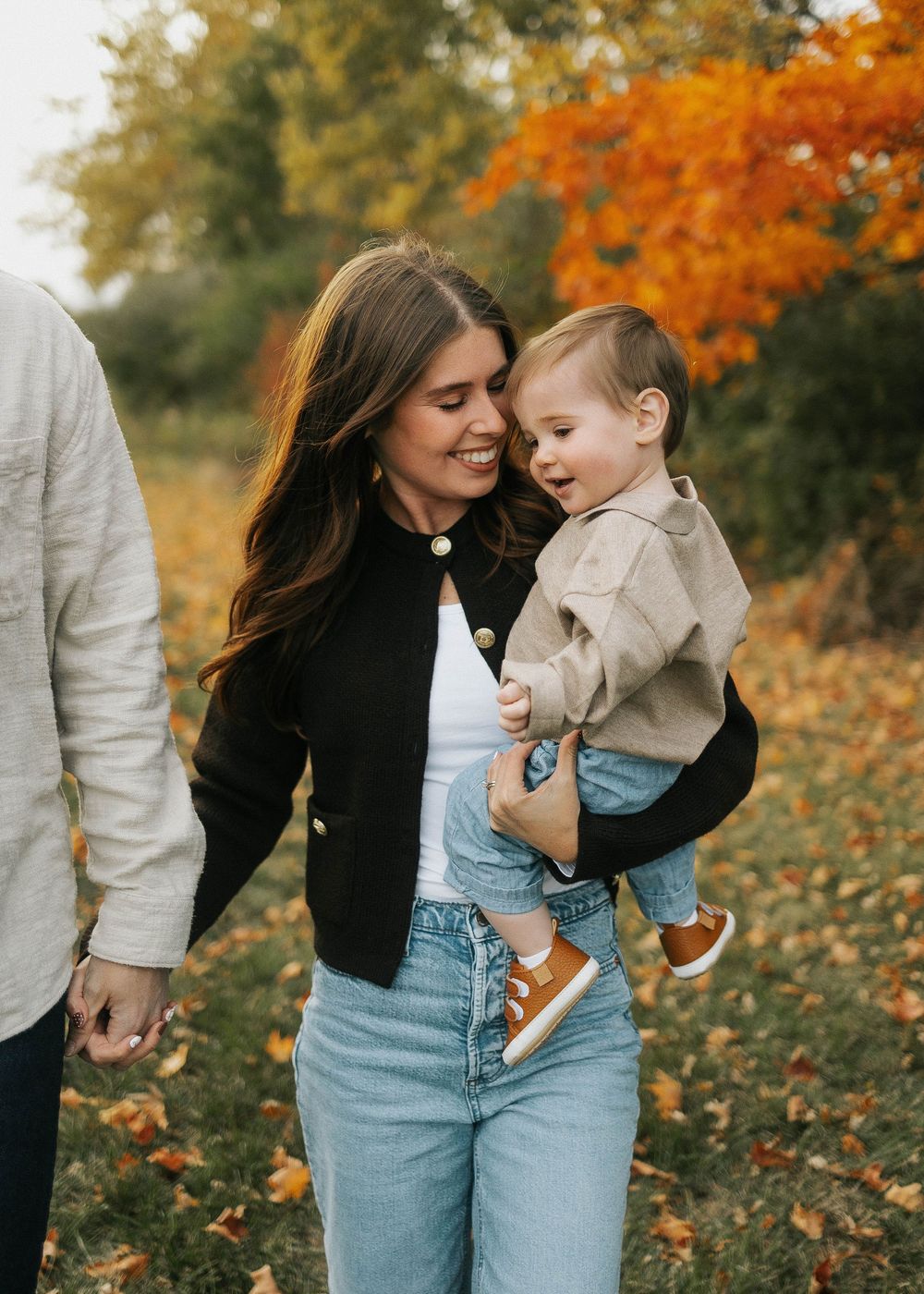 A parent and child share a tender moment outdoors among vibrant autumn foliage and fallen leaves.