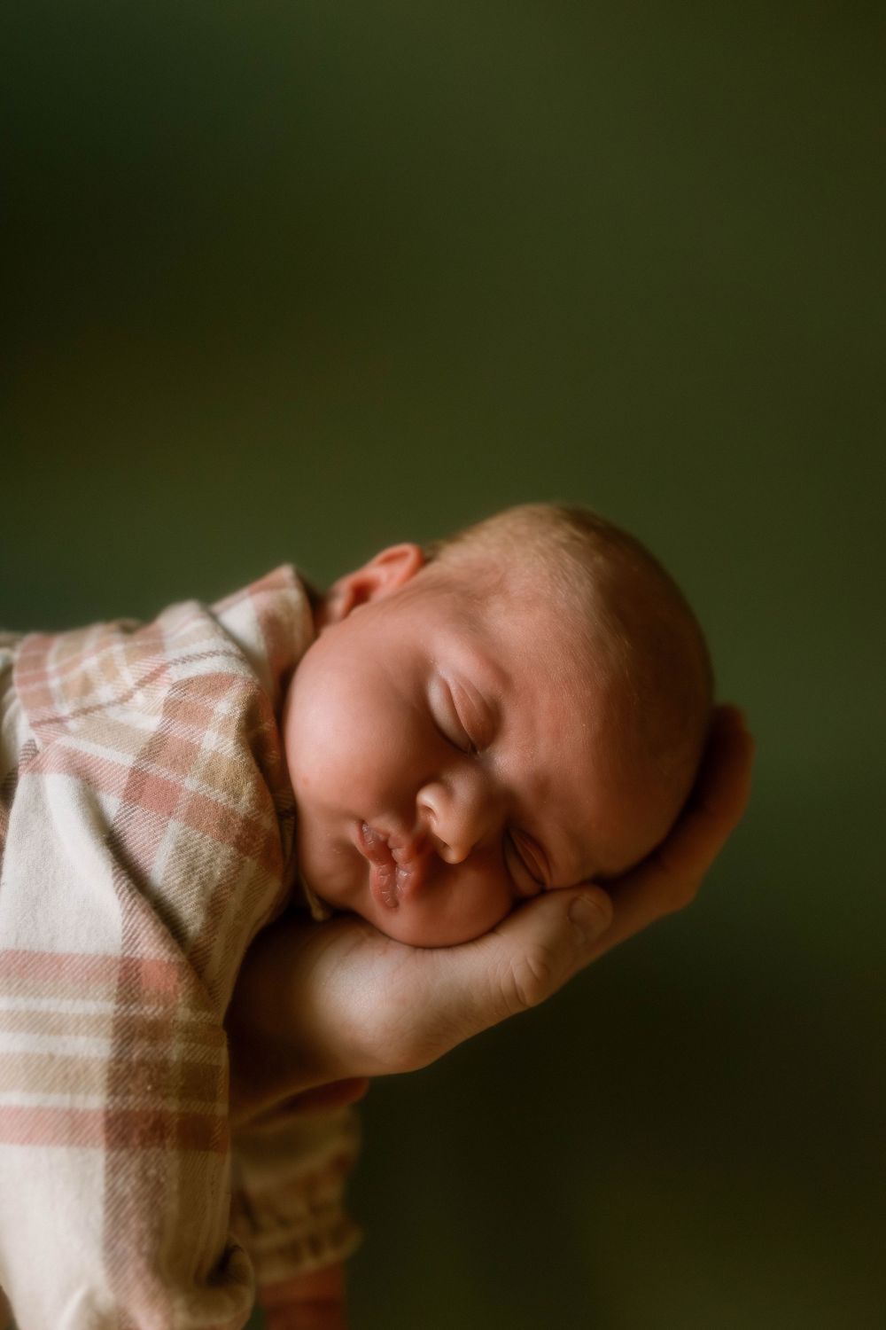 A peaceful sleeping infant rests on a supportive hand against a dark green background.