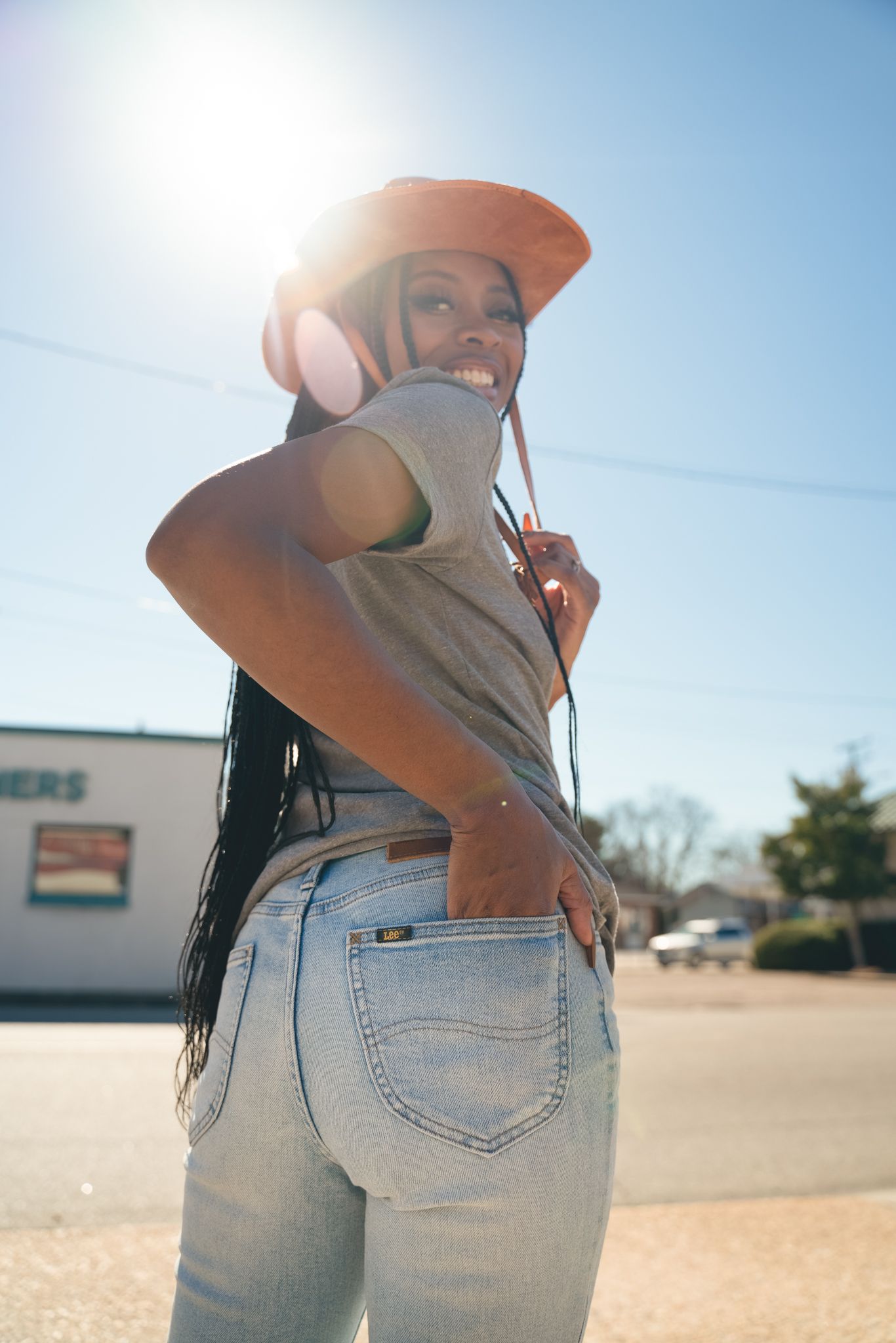 Person in an orange hat and light gray t-shirt poses outdoors on a sunny day wearing light wash jeans.