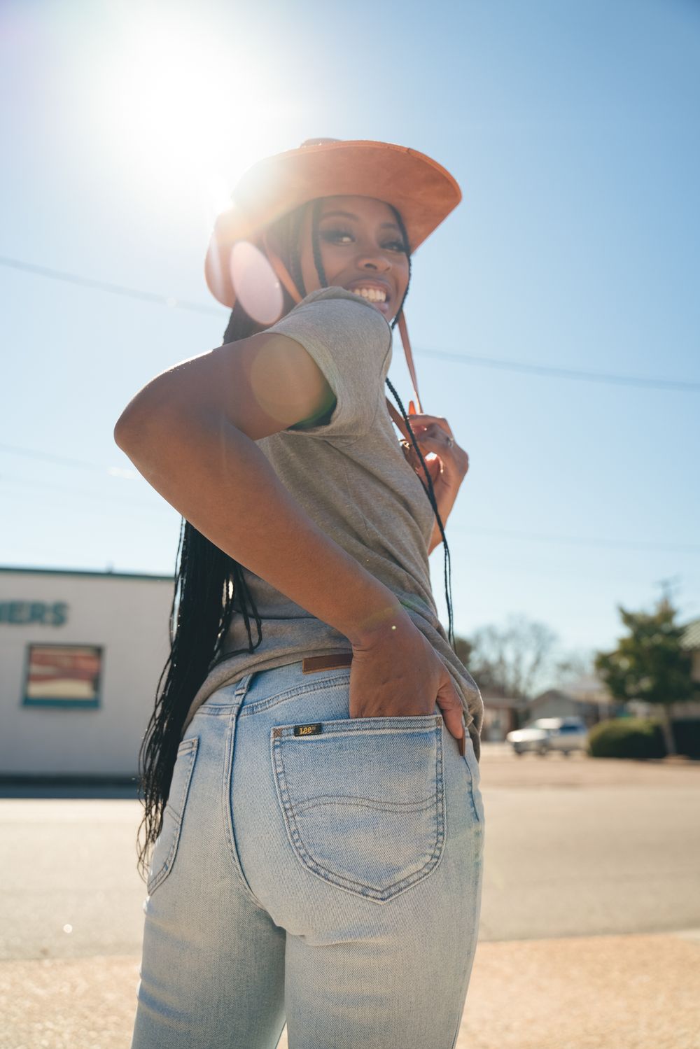 Person in an orange hat and light gray t-shirt poses outdoors on a sunny day wearing light wash jeans.