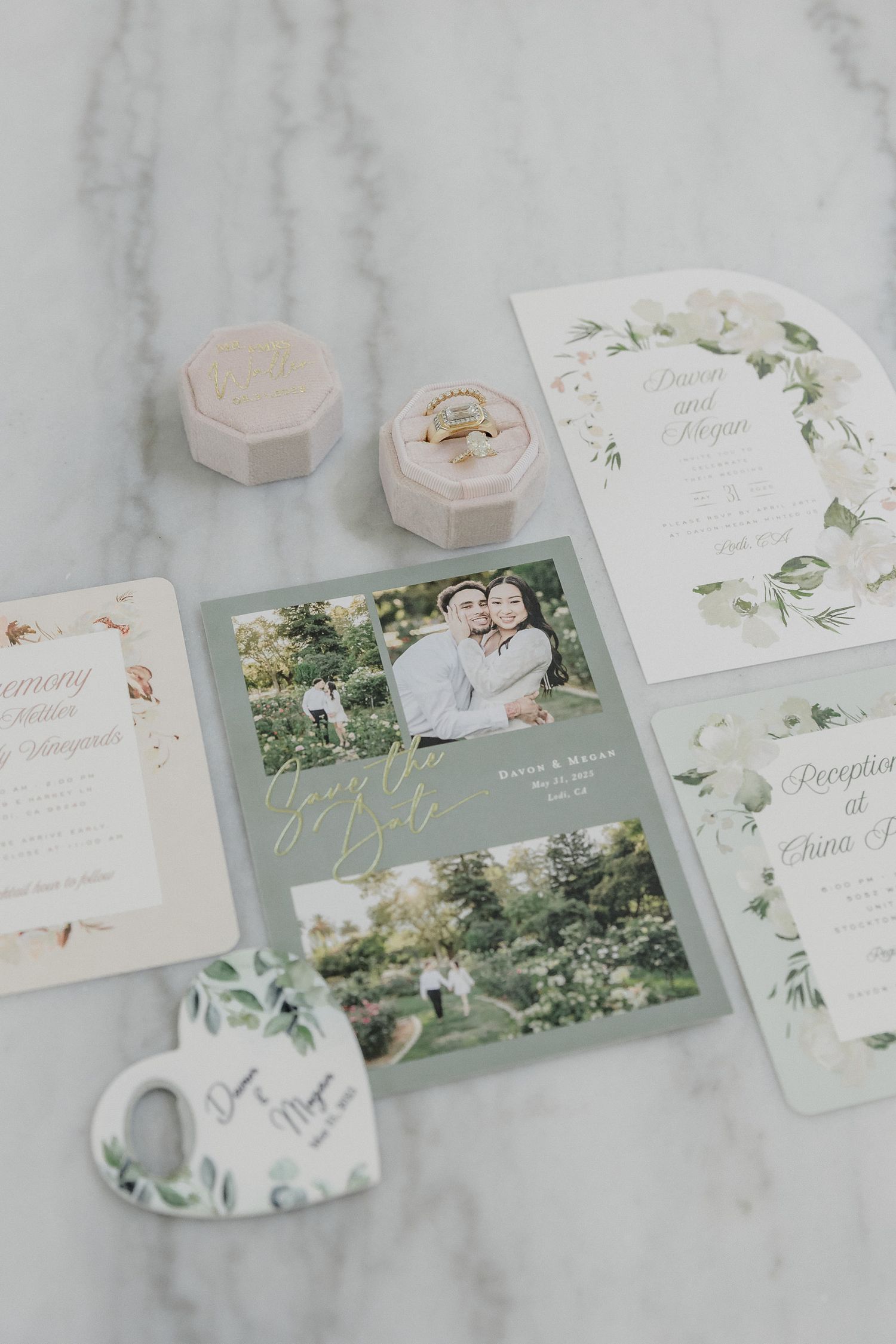 Elegant wedding stationery suite with invitation cards, velvet ring boxes and floral designs on marble background.