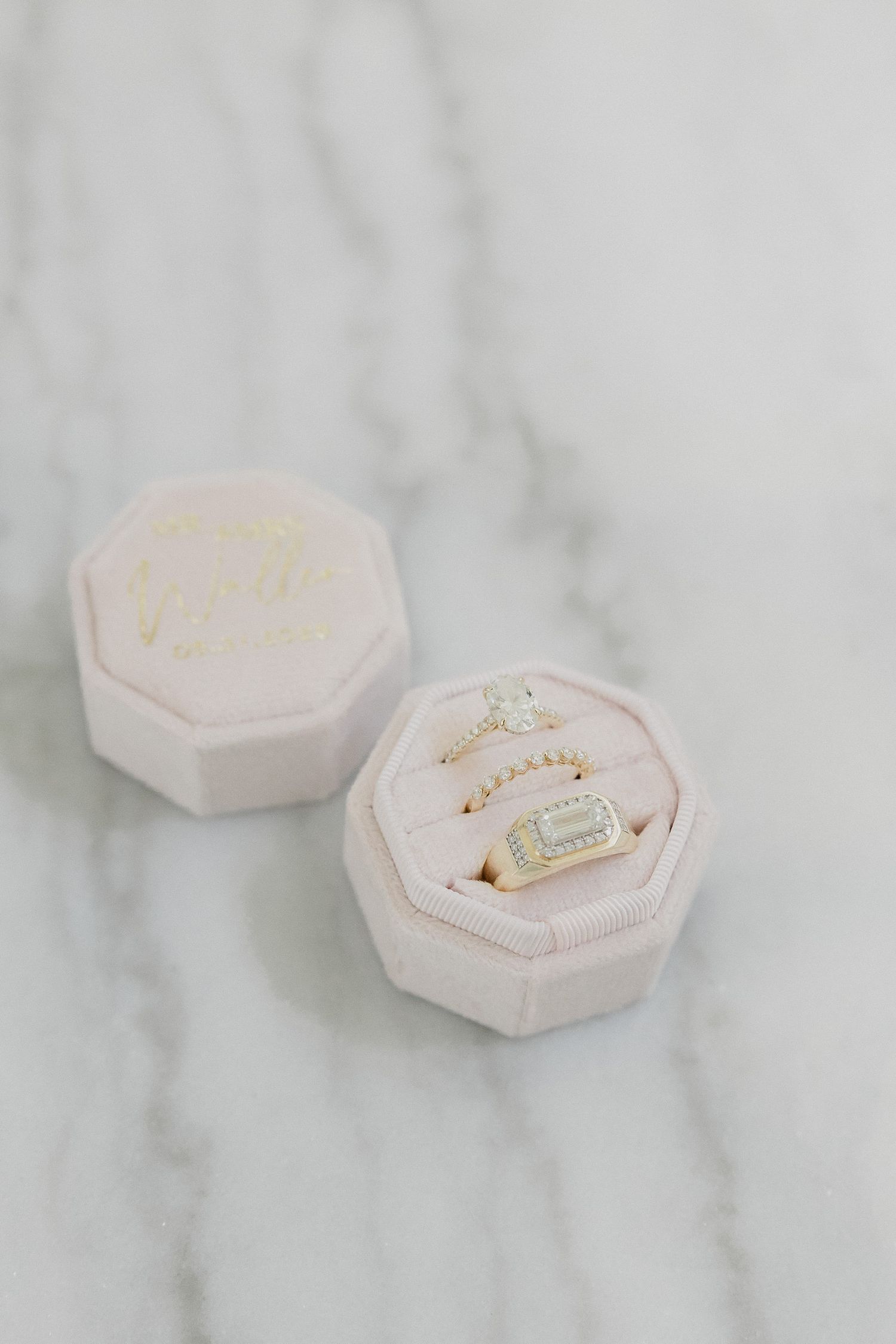Two pale pink octagonal jewelry boxes with delicate gold necklaces displayed on marble surface.