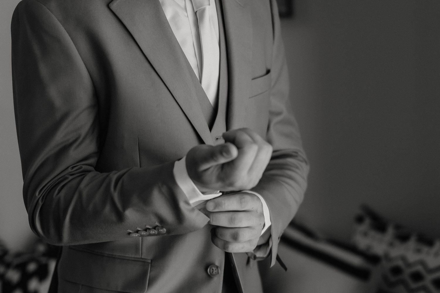 Black and white photo showing hands adjusting suit cuff buttons in elegant close-up detail.