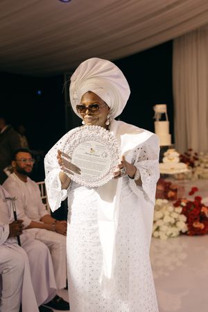 Guest at Nigerian wedding performing traditional raising of the gele headwrap ritual during the celebration ceremony.