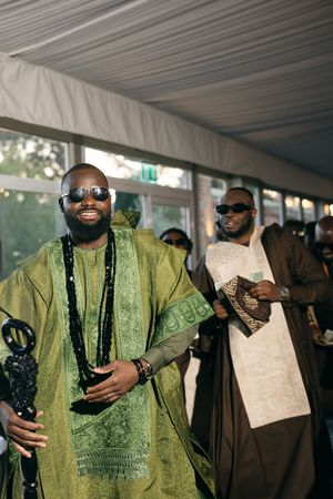 Two people in sunglasses wearing traditional African attire in vibrant green and cream colors at an outdoor event.