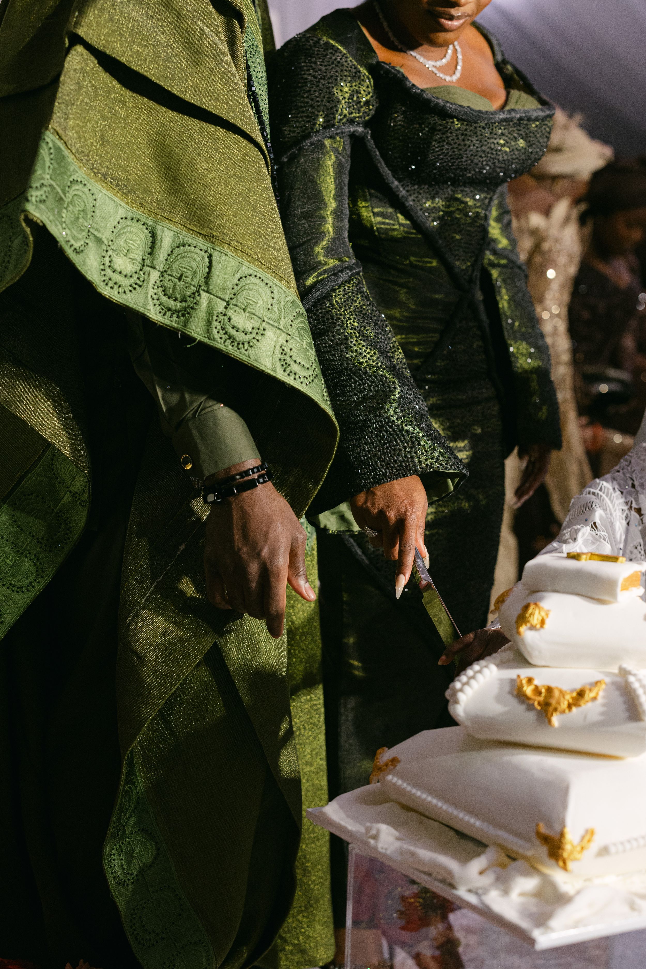 Close-up of elegant green and black traditional Nigerian wedding attire with a white tiered cake.