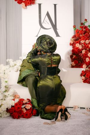 Emerald green evening gown with dramatic train laid out on floor with red and white floral decorations.