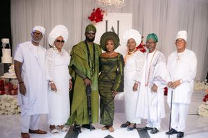 A group of people pose in formal attire with some wearing all white traditional clothing and two in green outfits at an event.