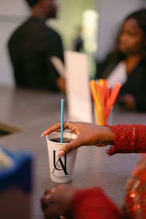 A hand holding a branded drink cup with a blue straw at an event reception.
