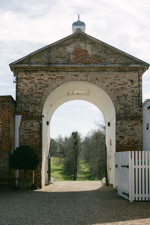 Historic brick carriage house entrance with white arched doorway and gravel path leading through multiple matching archways.