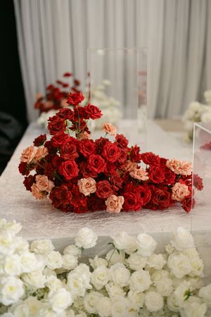 Beautiful floral arrangement with red and blush pink roses cascading over white roses in an elegant event setting.
