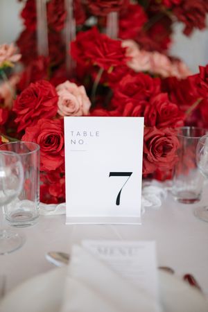 Wedding reception table number seven card displayed with red and pink roses and glass table settings.