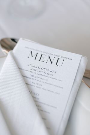 A close-up view of an elegant white menu card listing hors d'oeuvres and mains courses on a white linen napkin.