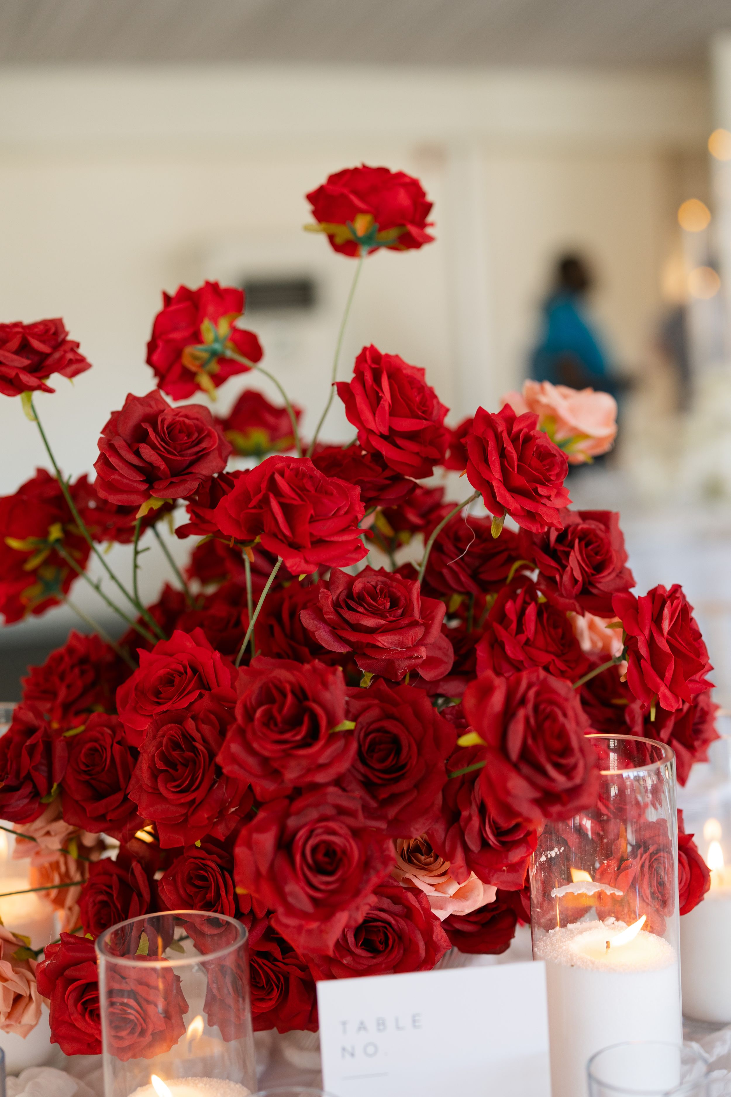 A lush centerpiece of vibrant red roses arranged with glowing votive candles on an elegant white table setting.