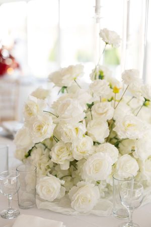 Elegant white roses arranged in low centerpieces with glass votives create a sophisticated wedding tablescape.