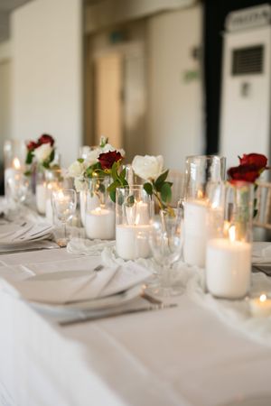 Elegant white table setting with glowing candles and red and white roses in glass vases for romantic dining.