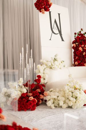 Elegant wedding backdrop with white drapes adorned with red and white floral arrangements and tall candles.