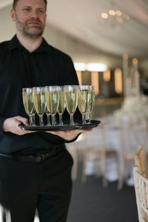 Staff member in black attire carrying a tray of champagne flutes at an elegant event.
