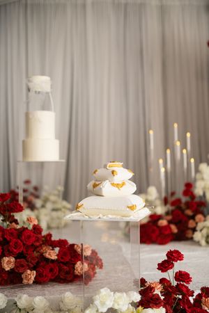 Elegant white wedding cake display surrounded by red and white roses with tall candles on a reflective surface.