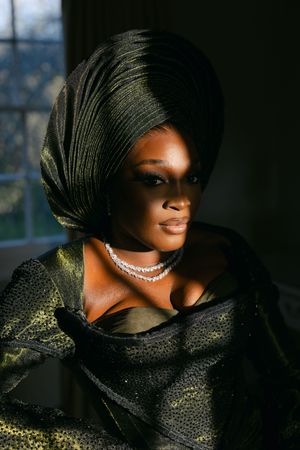 Dramatic portrait featuring an elegant look with black headwrap, diamond necklace and shimmering gold and black evening attire.