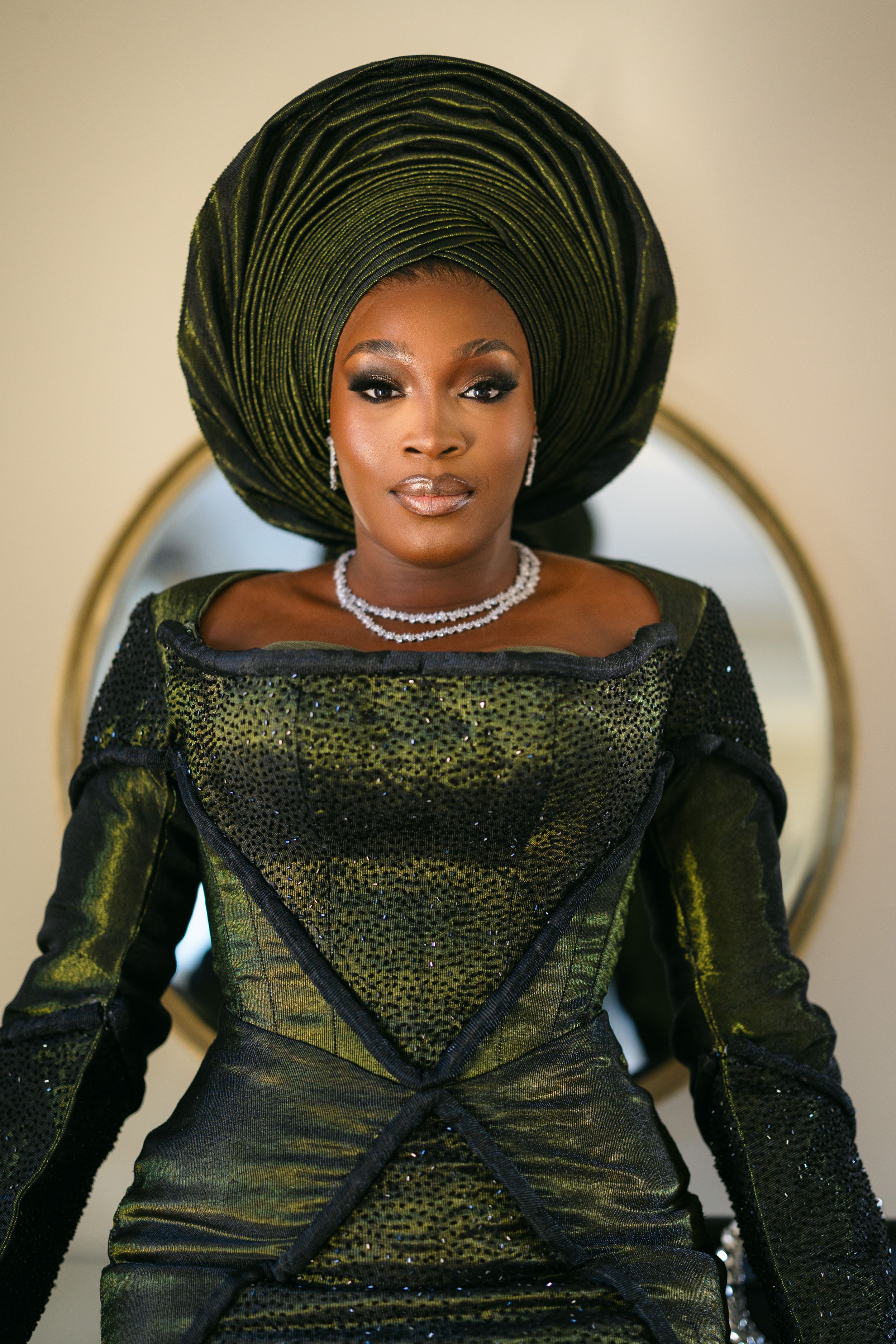 A traditional Nigerian gele headwrap in emerald green coordinates with a shimmering formal dress and diamond necklace.