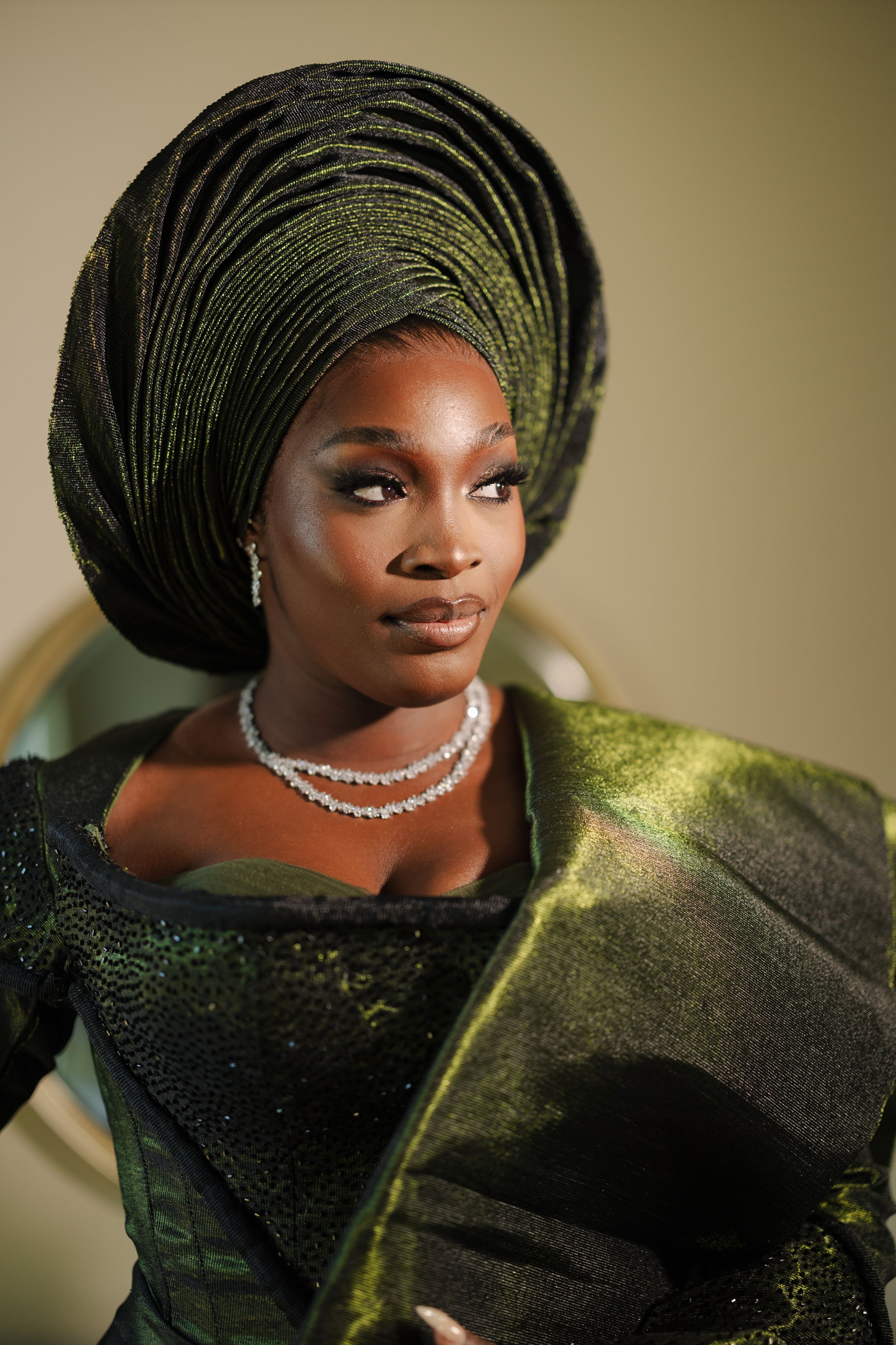 Elegant portrait featuring traditional African gele headwrap in dark green with shimmering fabric and diamond necklace.